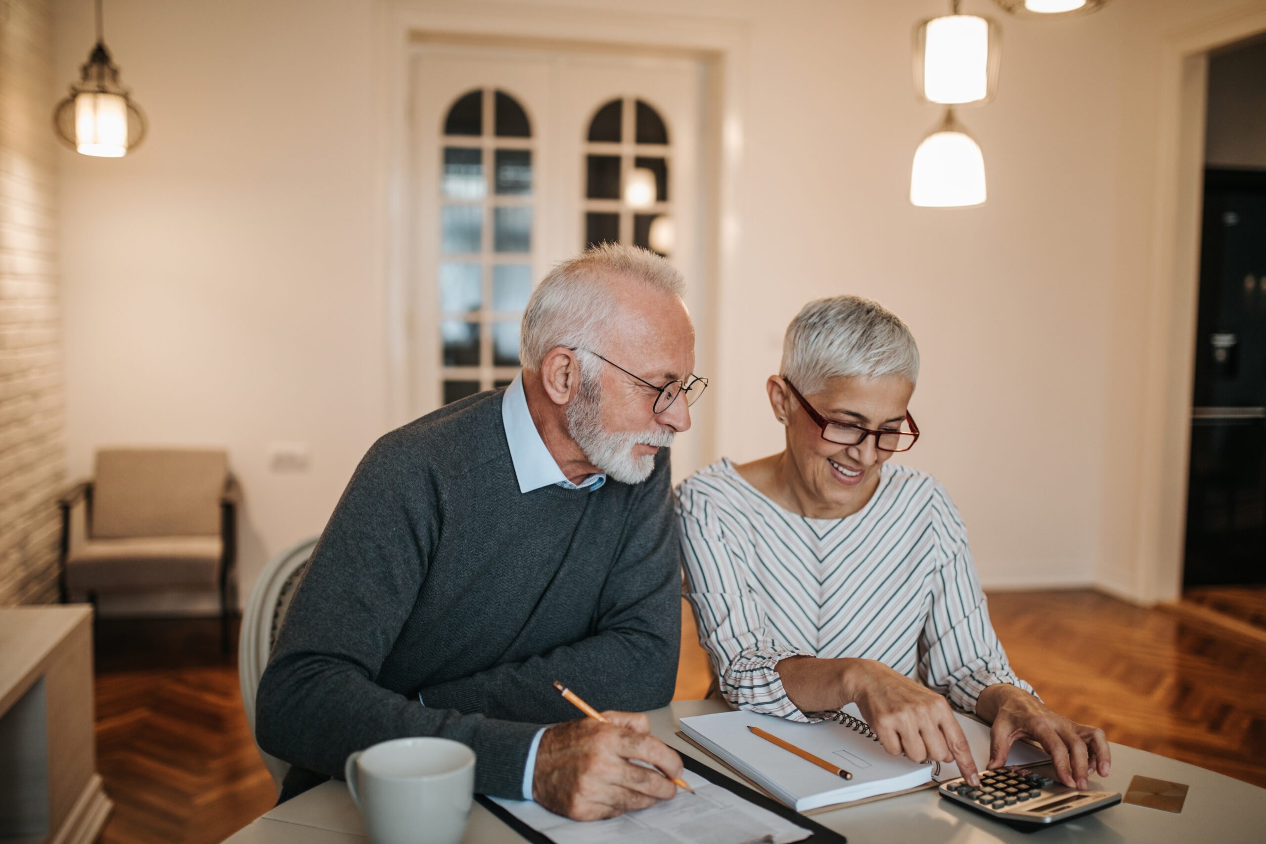 Retirement Planning Services | A happy senior couple calculating their finances in a beautiful home.